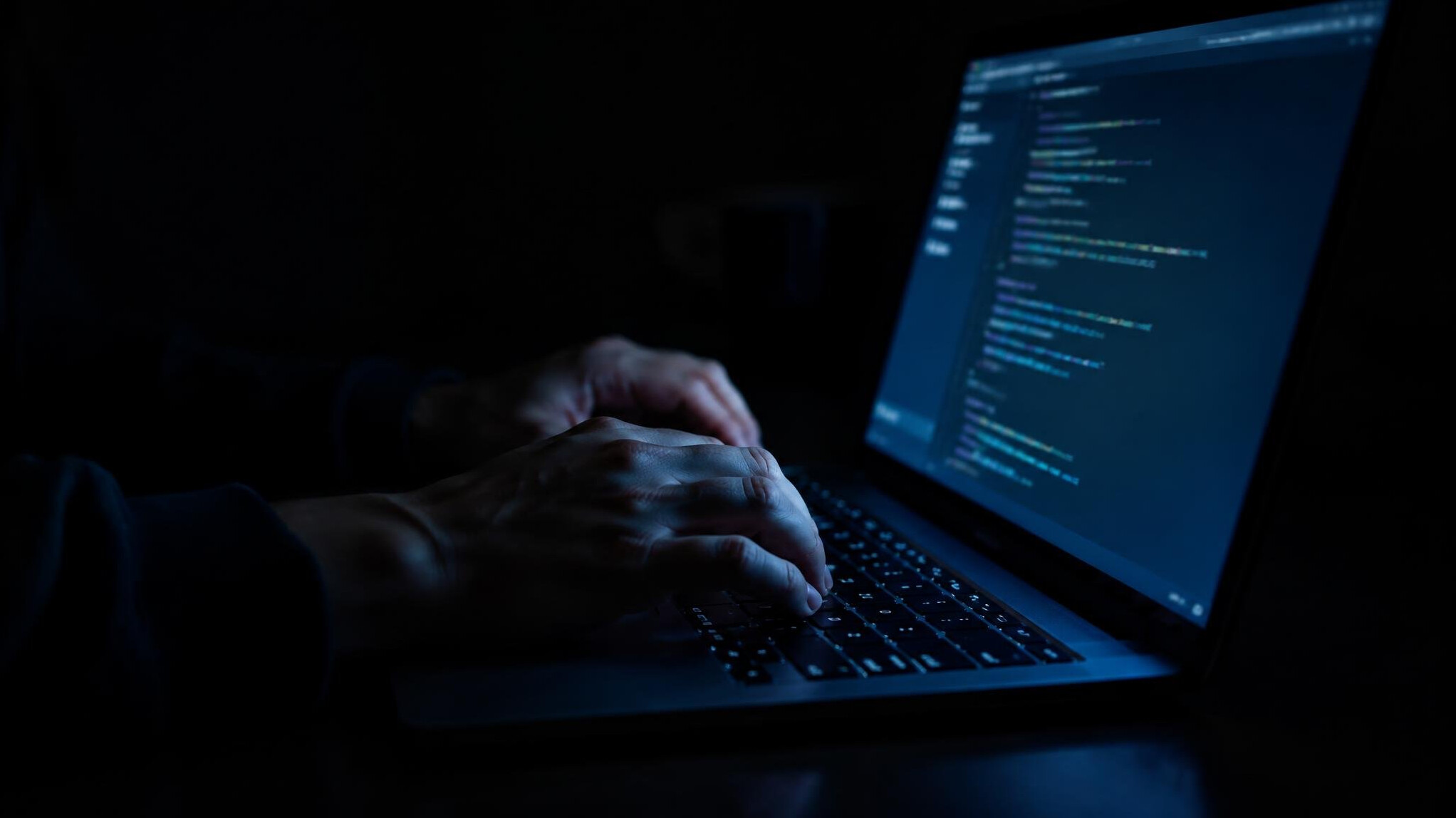 Person typing on a laptop in a dark room with only screen light